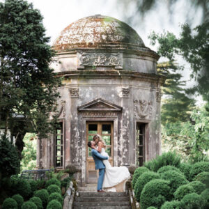 A bride and groom kissing in front of an old building, by Paul Gregory